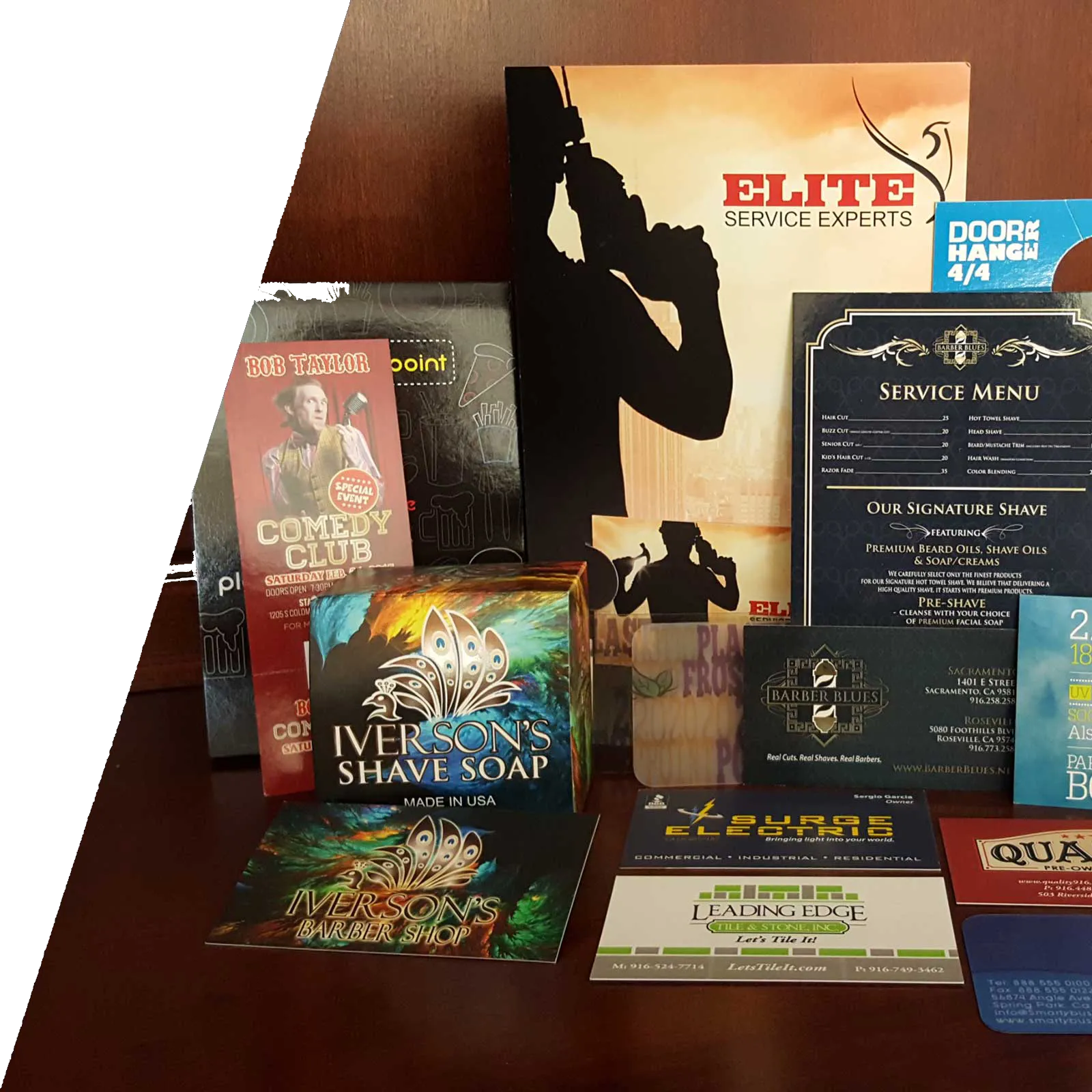 Flat-lay of small-format print work including business cards, menus, brochures, and product packaging for Barber Blues, Iverson's, and other clients