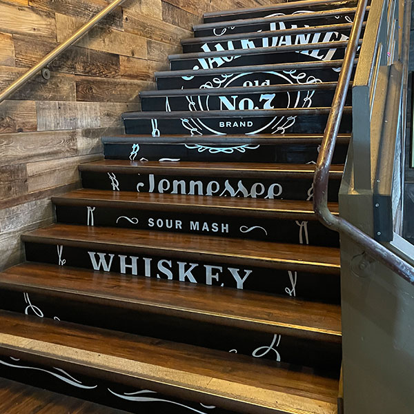 Jack Daniel's themed stair riser graphics installed on a wooden staircase in a bar interior
